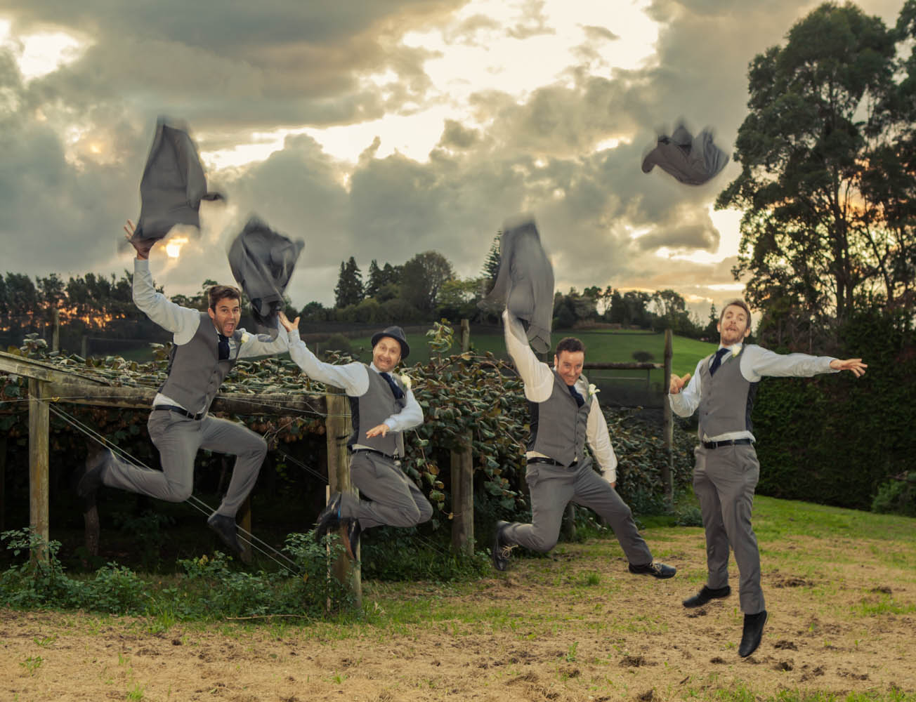 groom and groomsmen leaping in front of kiwifruit vines